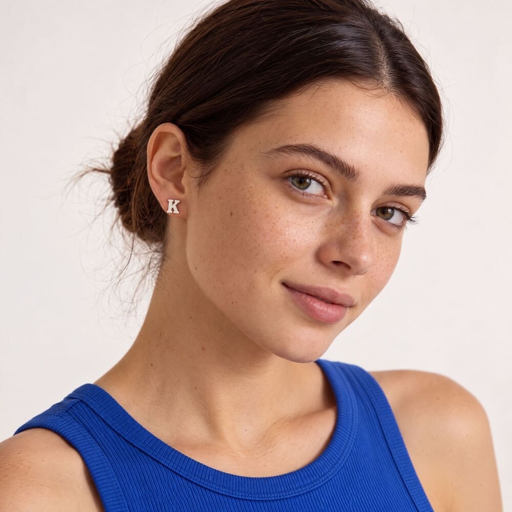 Modelo luciendo pendientes de letra K, con una camiseta azul