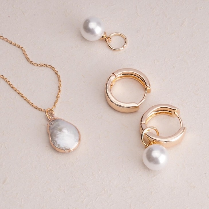 Close-up view of gold hoop earrings with dangling pearl accents and necklace