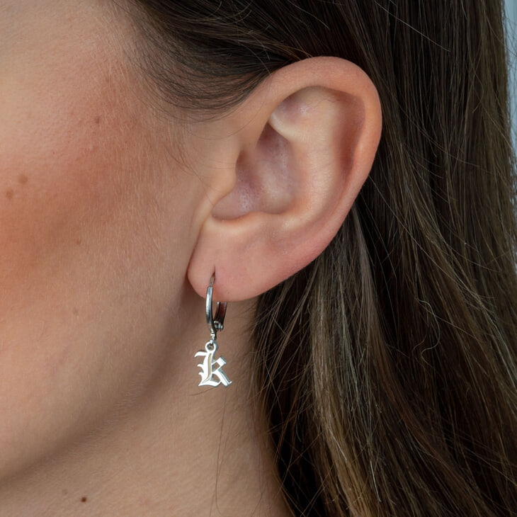 Modèle portant une boucle d'oreille gothique avec une initiale, ajoutant du caractère.