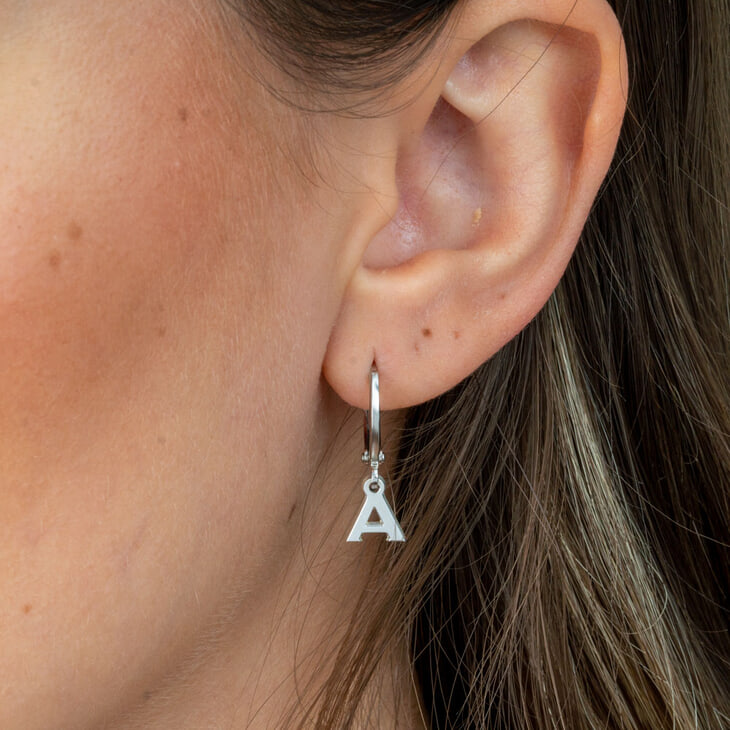 Modelo usando un arete colgante con la letra A, añadiendo un toque moderno a su look.