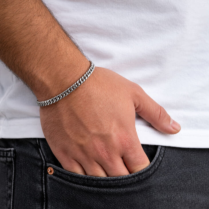Pulsera de eslabones cubanos plateada llevada en la muñeca de un modelo junto a su bolsillo