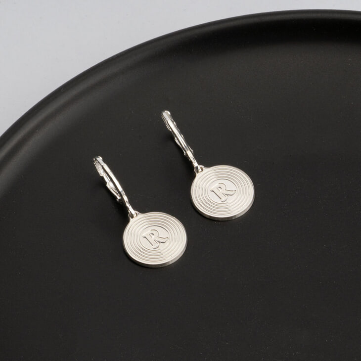 Detail shot of drop earrings with initial R displayed on a dark dish