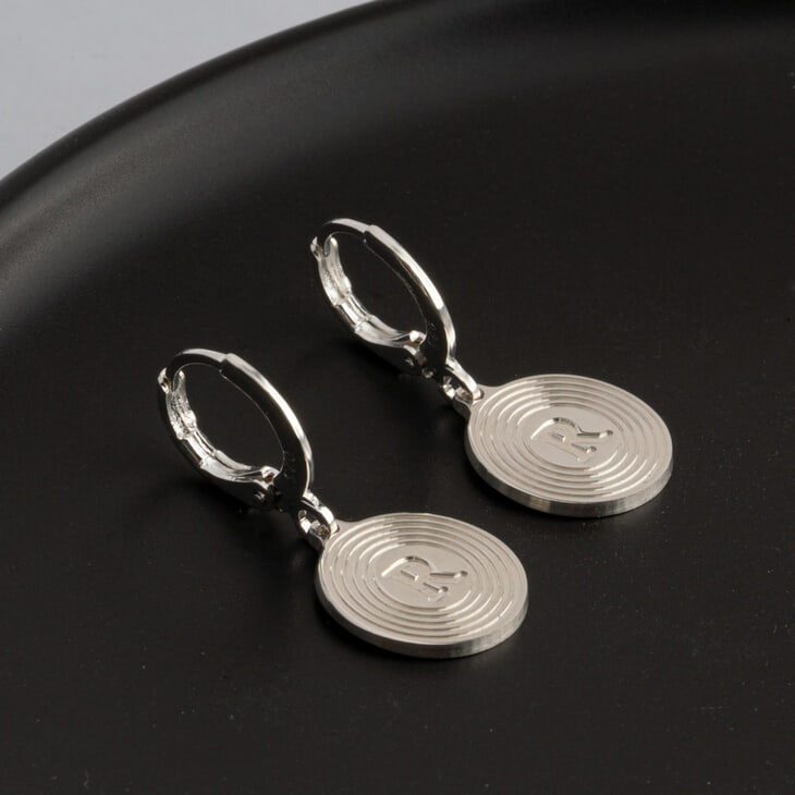 Close-up of personalized drop earrings featuring initial R on a black dish