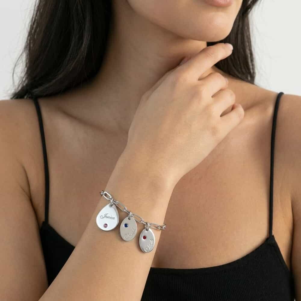 Silver personalized name and birthstone drop charm bracelet worn on a model's wrist.