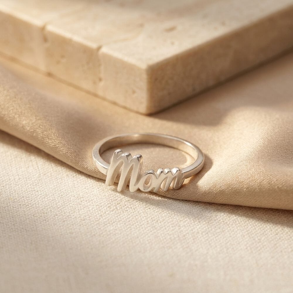 Anillo Dainty Mom colocado sobre una tela suave, resaltando su diseño encantador