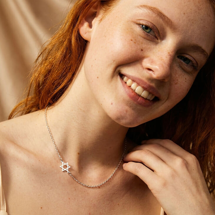 Woman with a joyful expression wearing the Sideways Star of David Necklace, highlighting its stylish design.