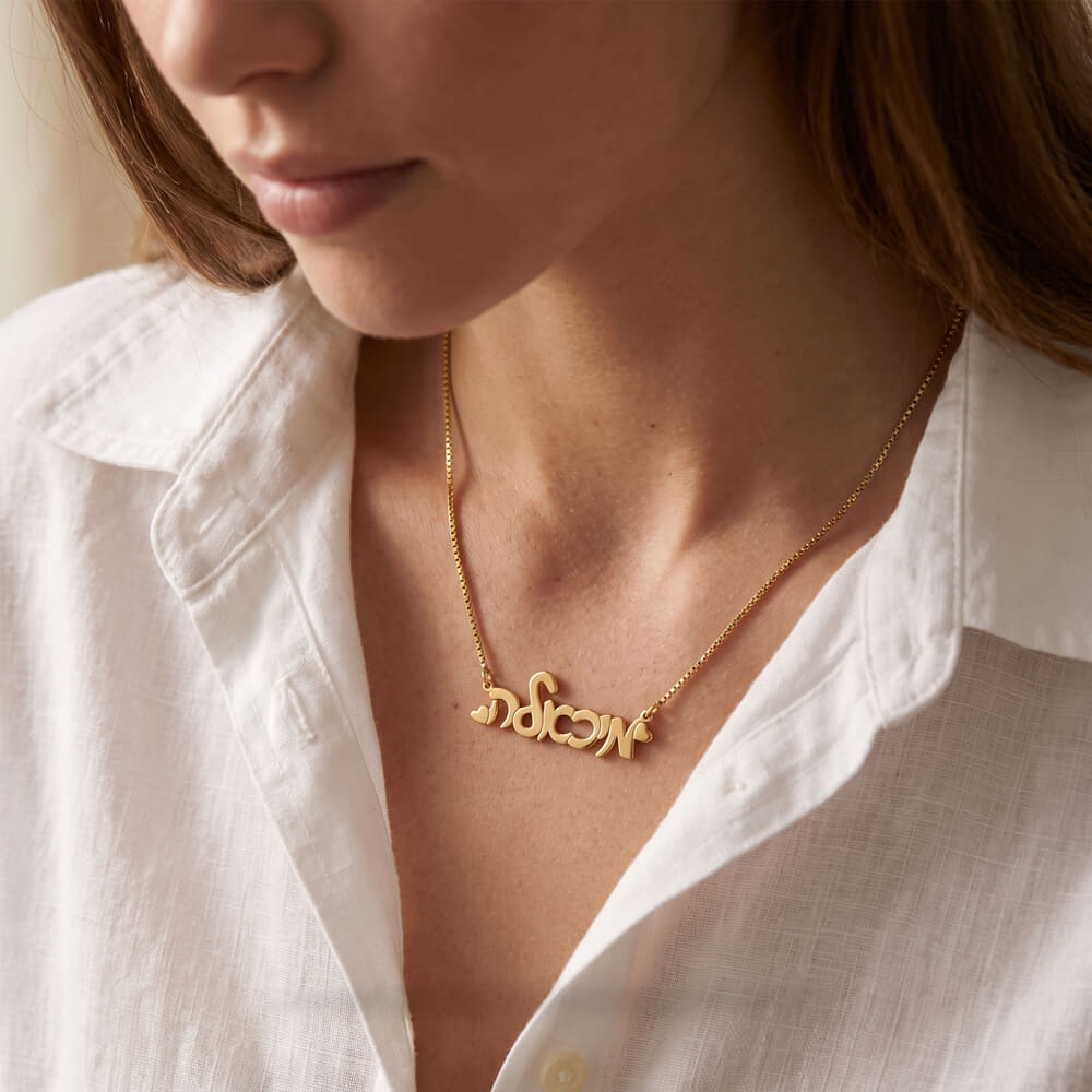 Model showcasing a cursive Hebrew name necklace with hearts, styled elegantly over a white shirt
