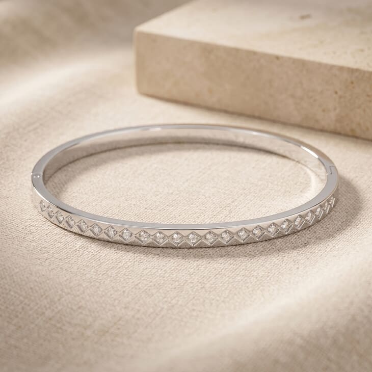 Close-up of a geometric bangle with cubic zirconia on a textured surface