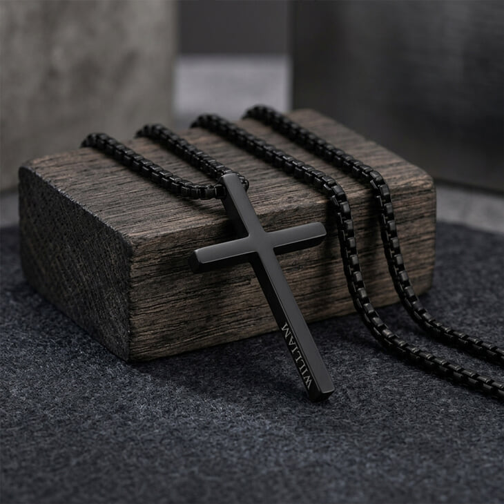 Men's Black Cross Necklace resting on rustic wood with name engraving